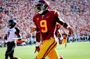 [Image description: A football player wearing a red and yellow uniform that reads the number 9. Behind him are some other football players, some wearing the same and the one wearing a green and yellow uniform.]