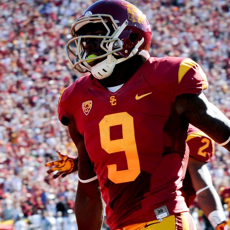 [Image description: A football player wearing a red and yellow uniform that reads the number 9. Behind him are some other football players, some wearing the same and the one wearing a green and yellow uniform.]