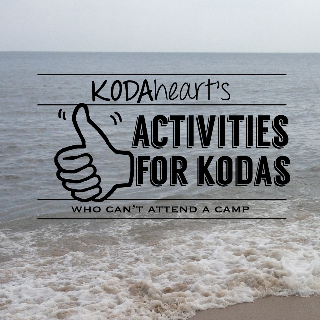 [Image Description: A thumb, outlined in black, signs “10” with accompanying text that reads: “KODAheart’s [10] Activities for kodas who can’t attend a camp”. In the background is a picture of the ocean, with a wave gently crashing on the beach.]