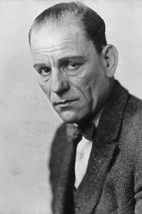 [Image Description: A black and white image of an aged white man in a suit and bow-tie. His hair is neatly combed back and he looks up at the viewer with a somber expression.