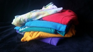 Image Description: A group of different colored t-shirts are stacked vertically on top of a black background. 