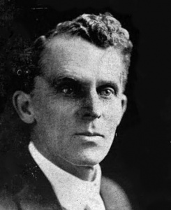 Image Description: A black and white portrait of a clean-shaven white man in a suit and tie.]