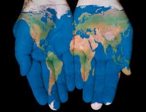 [Image Description: Two hands side by side palms up with an image of the world and its continents and oceans “painted” on.]