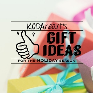 Image description: A thumb, outlined in black, signs “10” with accompanying text that reads: “KODAheart’s [10] gift ideas for the holiday season.” In the background is a closeup colorfully wrapped boxes with ribbon bows.