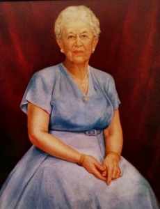 Image description: This painted portrait shows Elizabeth Peet seated with her hands clasped in her lap. She is wearing a belted blue dress and a long necklace. Her white hair is pulled back and she looks out from the painting with a calm smile.