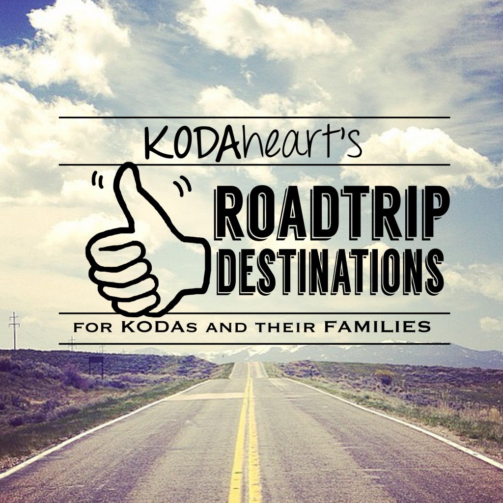 [Image Description: A thumb, outlined in black, signs “10” with accompanying text that reads: “KODAheart’s [10] Road Trip Destinations for KODAs and their families. In the background, an open highway trailing off into the distance with a cloud filled blue sky overhead.]