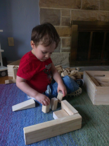 Image Description: A child wearing a red shirt and blue jeans sits in front of a fire place playing with wooden blocks