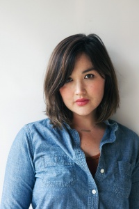 [image description: A portrait of a Chinese and white woman with shoulder-length dark hair. She is wearing a relaxed blue collared shirt with a red tank top underneath.]