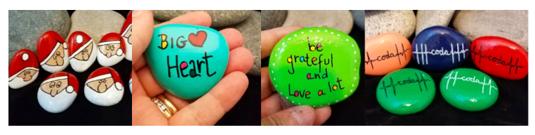 [Image description: In the first photo is of various shaped rocks painted with a Santa Claus face. The next photo is of a turquoise painted rock with the words “BIG Heart”. A heart shape is between the two words. Next is a green painted rock with “Be grateful and love alot” surrounded by little white dots. The void in the letters are filled in with different colors. The last photo is of orange, blue, red and green painted rocks with the word coda in the middle of a heartbeat line.]