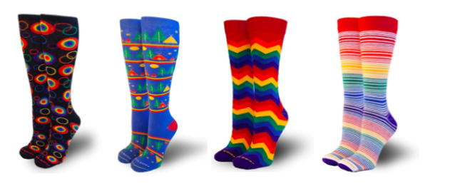 [Image description: Four pairs of colorful calf length socks are lined up. The first pair on the left side are black with primary colored circle outlines. Some of the circles are filled in with multiple rings. The second pair are blue with different campsite images with a tents and trees stacked up one on top of each other separated by a rainbow border. The next pair is a repeating primary color zigzag pattern. The last pair is horizontally striped with light and dark primary colors.]