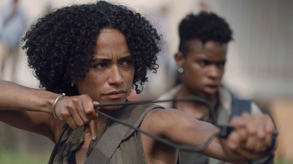 A black woman is pulling back and aiming a slingshot. 