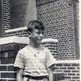 Image Description: A young white boy standing in front of a brick building looking off camera.