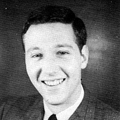 A black and white photo of a young McChord, wearing a dark suit, black tie, and a smile.